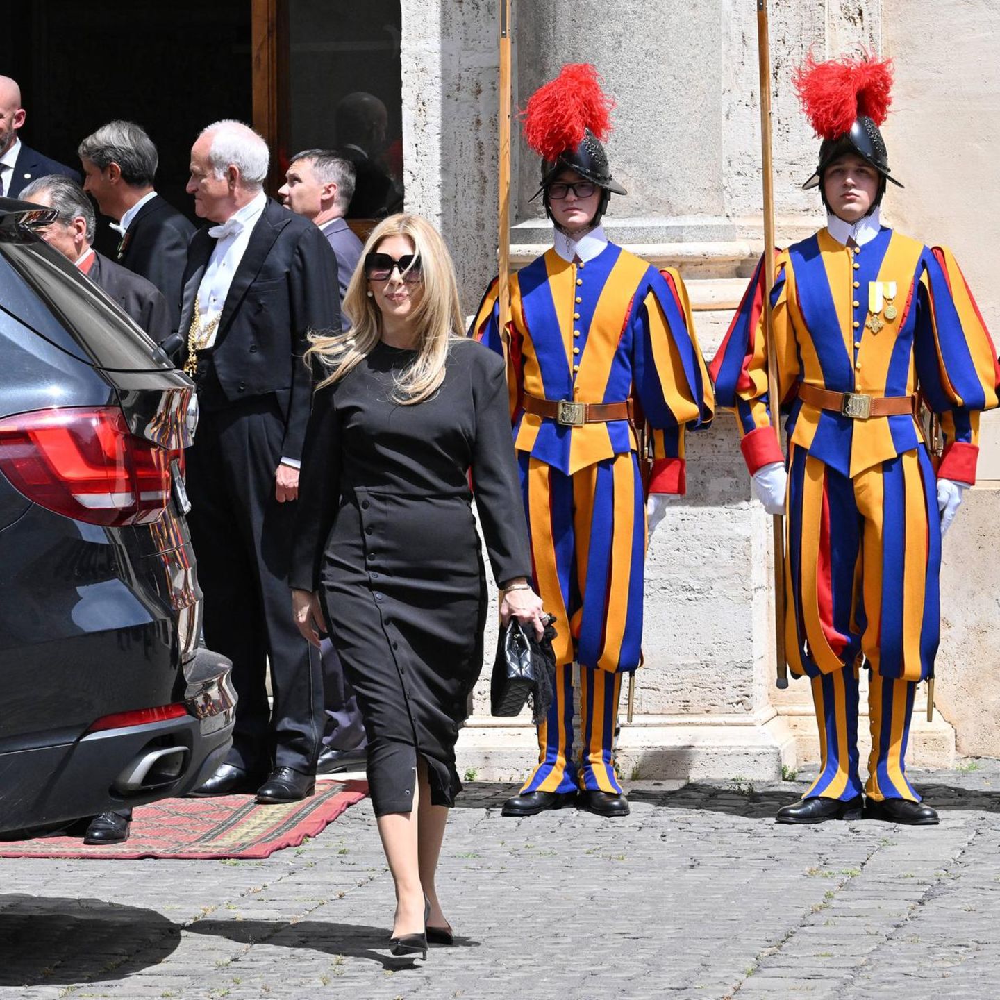 Apostolischer Palast, Vatikan. Jeanette Dousdebes Rubio kommt gerade von einem Treffen mit Papst Leo, dem XIV. Die Schweizer Gardisten stehen stramm. Rubio ist die Ehefrau des amerikanischen Außenministers Marco Rubio. Das Ehepaar ist strenggläubig. Man fragt sich immer, was sie wohl von den Pöbeleien Trumps gegen den Heiligen Vater halten?