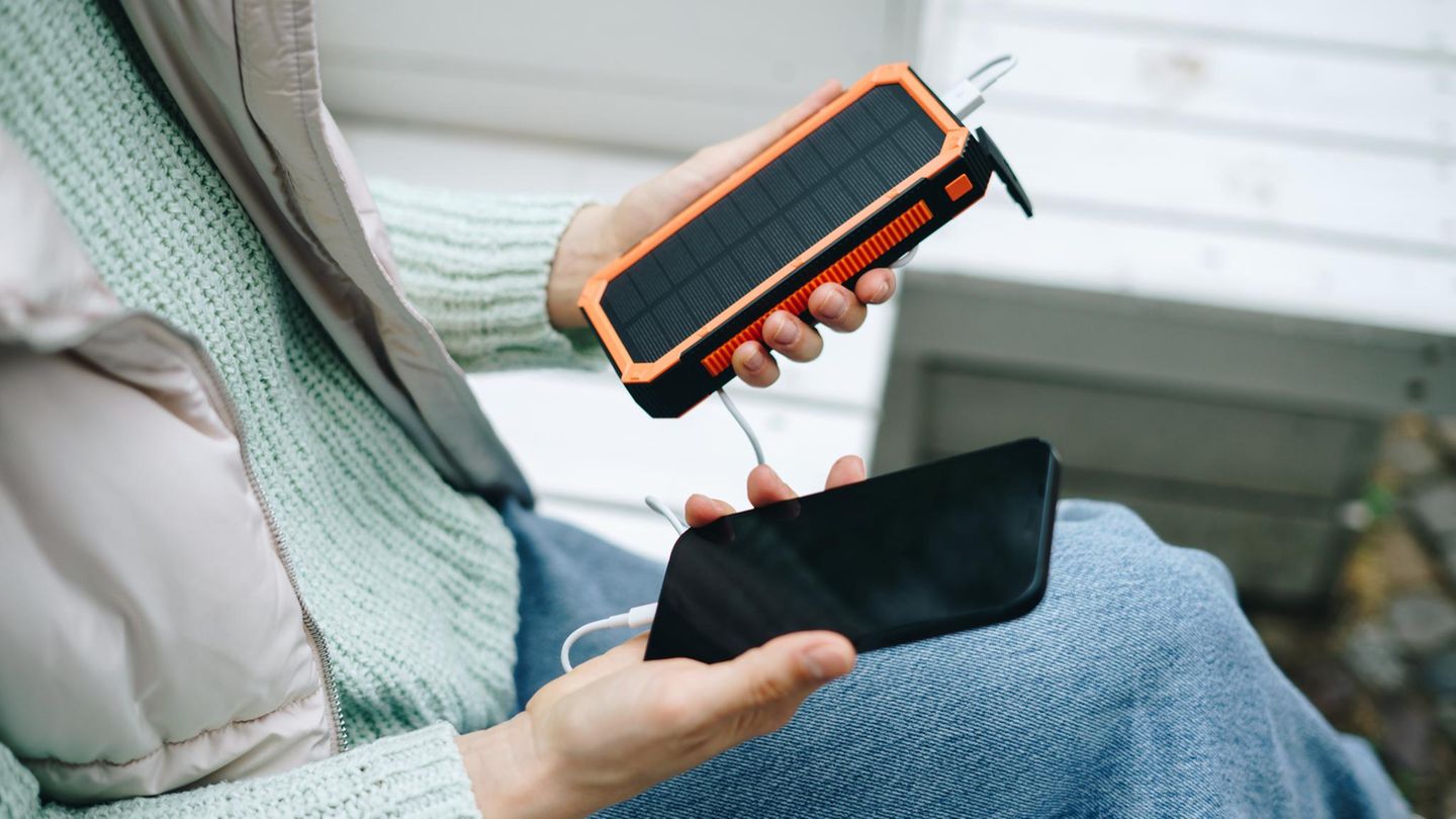 Frau lädt Smartphone von einer Solar-Powerbank im Freien auf