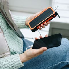 Frau lädt Smartphone von einer Solar-Powerbank im Freien auf