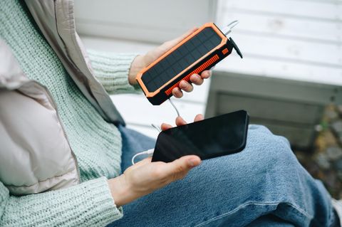 Frau lädt Smartphone von einer Solar-Powerbank im Freien auf