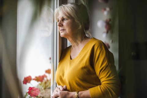 Eine ältere Frau blickt aus dem Fenster, sie ist besorgt