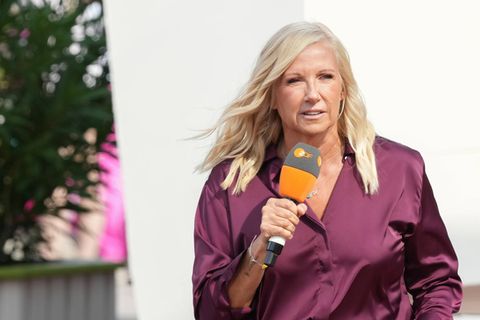Andrea Kiewel trägt eine Bluse und offene, gewellte Haare und hält ein Mikrofon in der Hand
