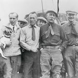 Nobile, der seinen Hund auf dem Arm hält, steht neben Ellsworth und Amundsen sowie weiteren Männern der Crew.