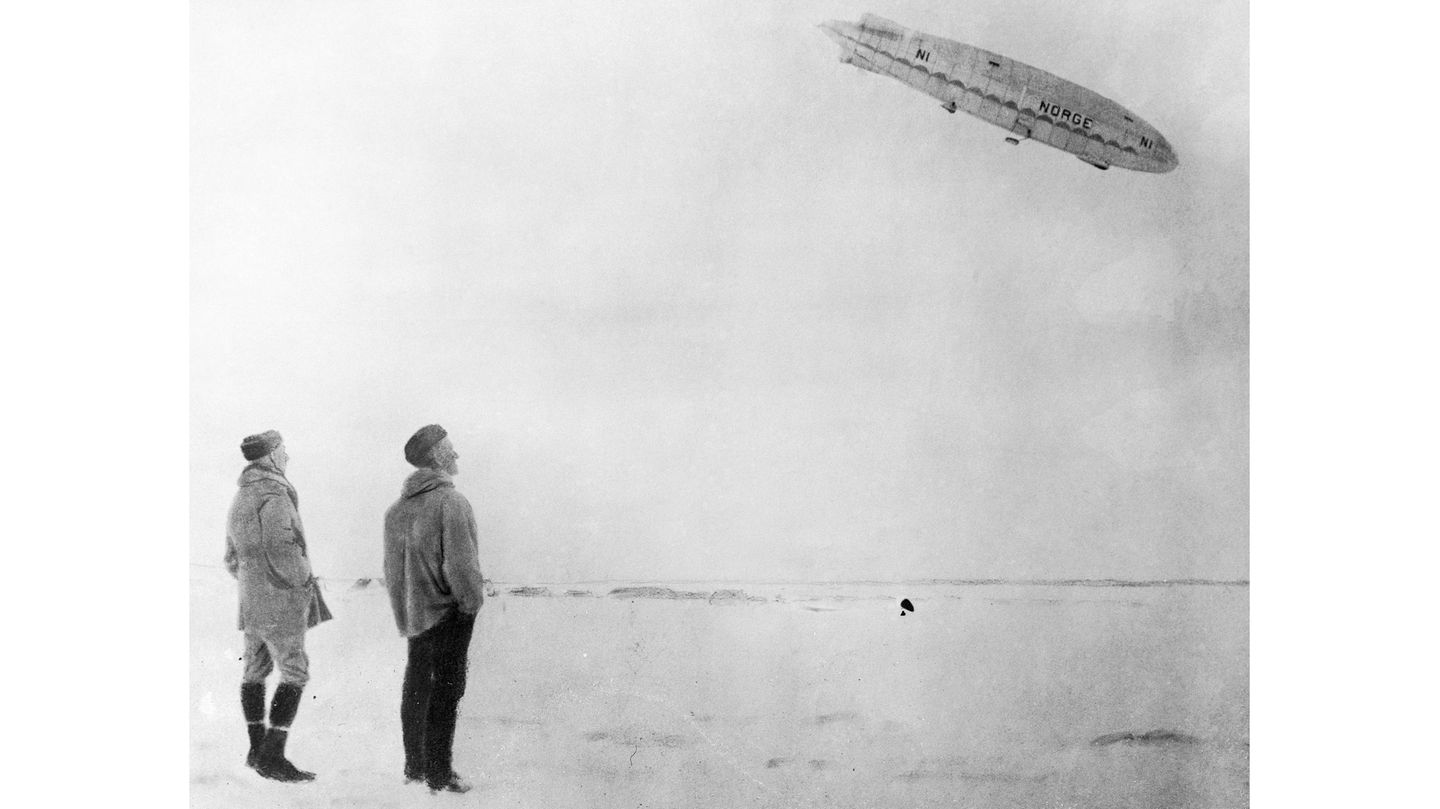 Amundsen und Ellsworth betrachten vom Boden aus die „Norge“ am Himmel.