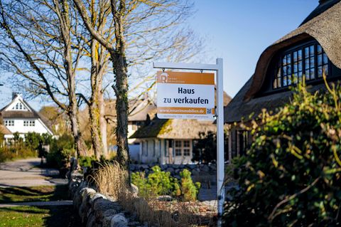 Ein Schild mit der Aufschrift  Haus zu verkaufen steht vor einem mit Reet gedecktem Haus im Ostseebad Ahrenshoop