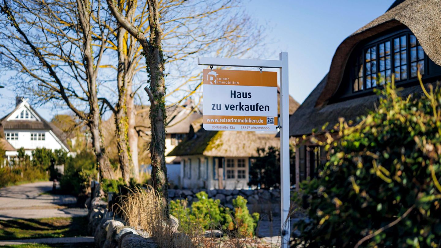 Ein Schild mit der Aufschrift  Haus zu verkaufen steht vor einem mit Reet gedecktem Haus im Ostseebad Ahrenshoop