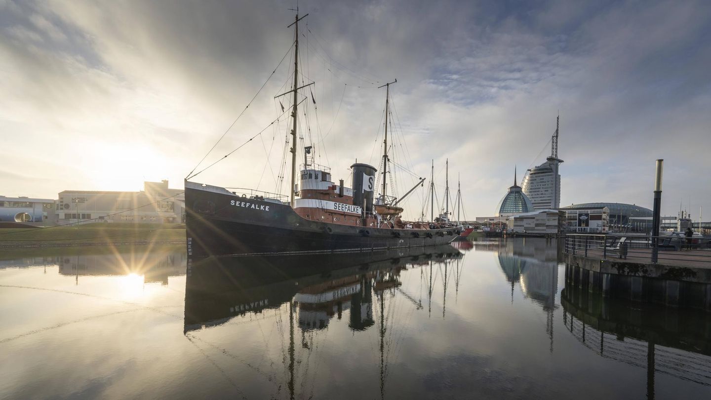 Ein Schiff im Hafen mit beeindruckender Spiegelung im Wasser bei Sonnenuntergang vor einer modernen städtischen Kulisse