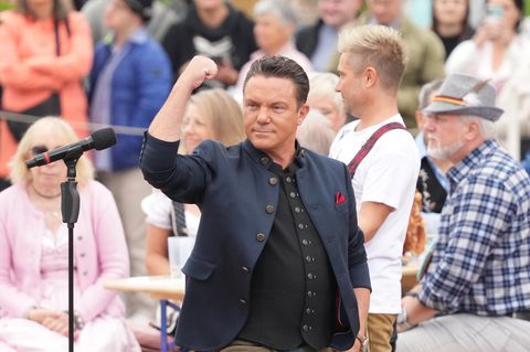 Stefan Mross steht vor einem Mikrofon und reckt den Arm in die Höhe