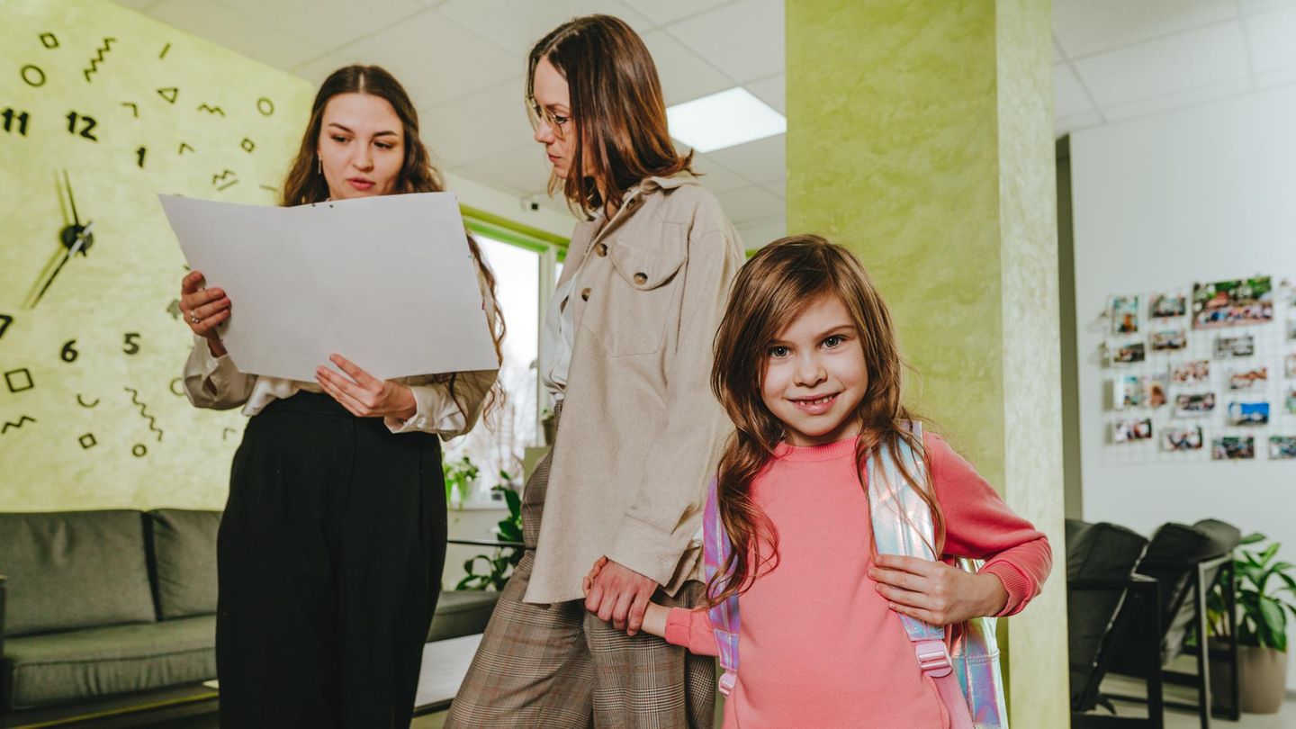 Schulnote: Lehrerin spricht mit Mutter, die ihr Kind an der Hand hält