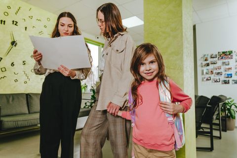 Schulnote: Lehrerin spricht mit Mutter, die ihr Kind an der Hand hält