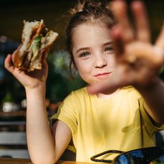 Ein Mädchen mit einem Burger in der Hand grinst glücklich