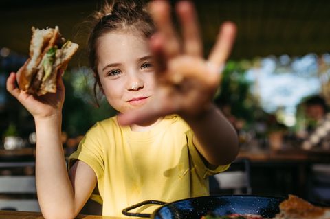 Ein Mädchen mit einem Burger in der Hand grinst glücklich