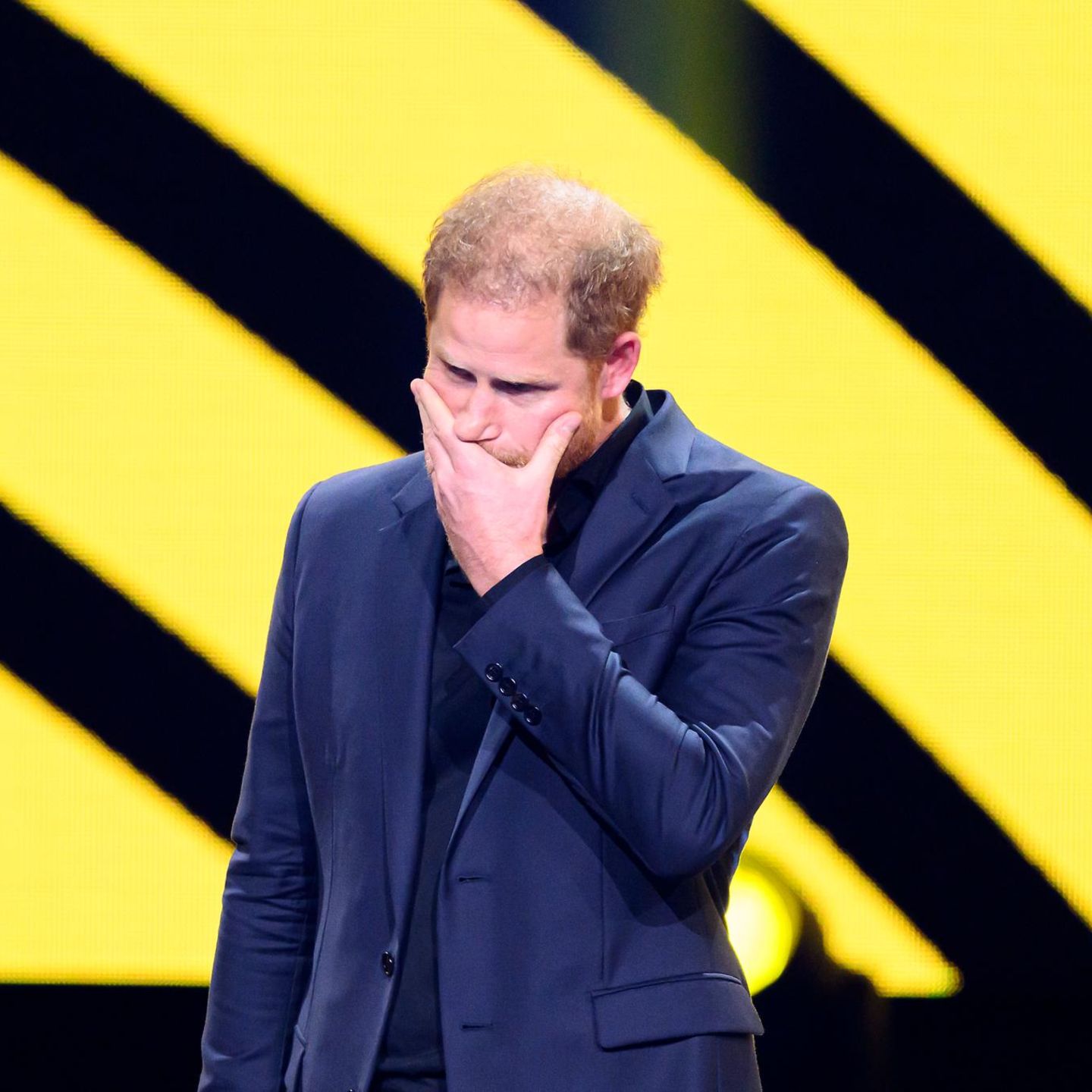Prinz Harry hält sich eine Hand vor den Mund