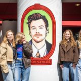 Vier Mädchen stehen vor einem gemalten Porträt von Harry Styles