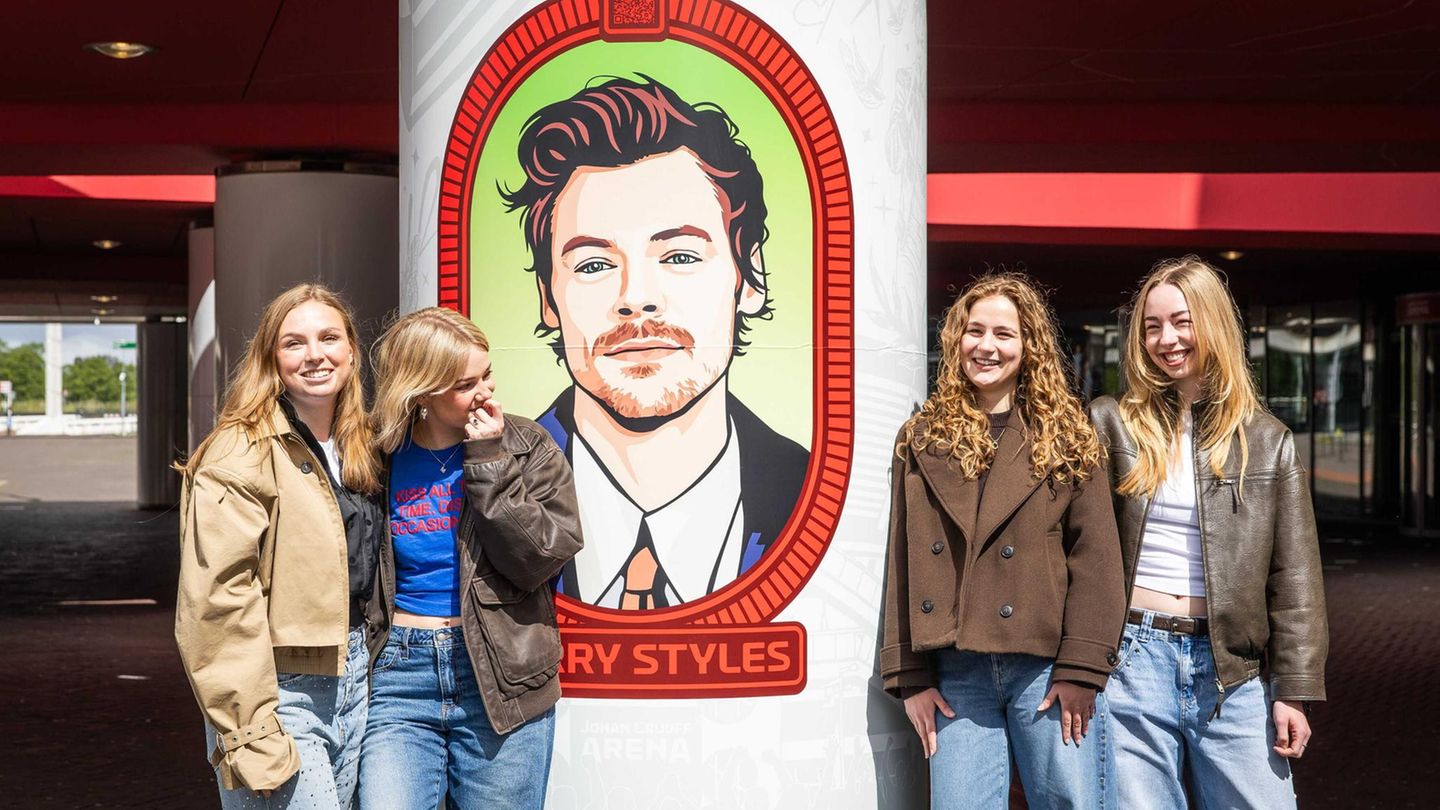Vier Mädchen stehen vor einem gemalten Porträt von Harry Styles