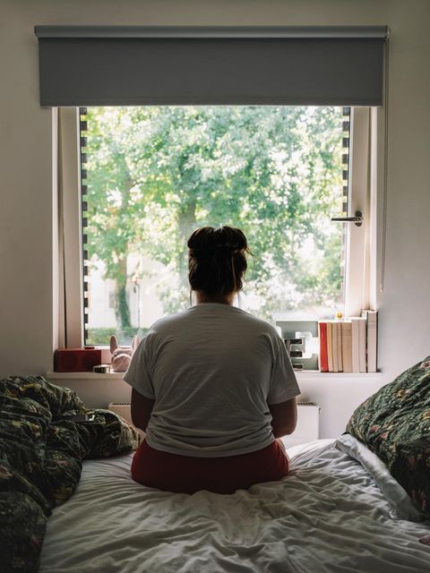 Unglücklich verliebt: Frau sitzt auf Bett und schaut aus dem Fenster