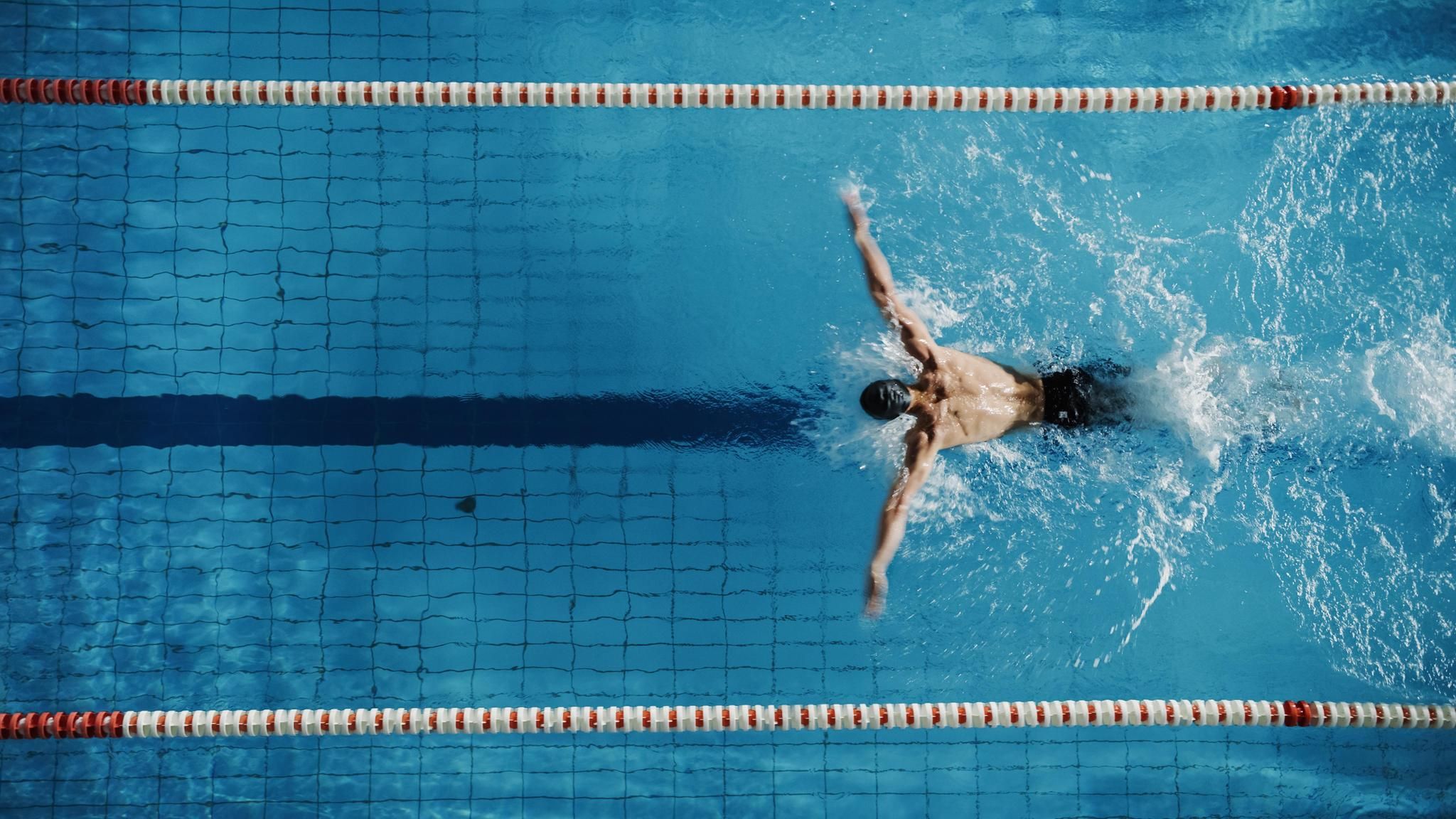 Vogelperspektive auf einen Mann, der im Delfin-Stil schwimmt