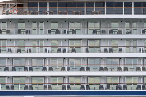 Auf dem Bild ist ein Kreuzfahrtschiff von Außen zu sehen. Auf den Balkonen stehen Stühle.