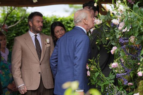 König Charles riecht an einer Blume, im Hintergrund steht David Beckham