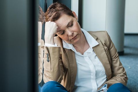 Thema Alkohol im Büro: Erschöpfte Frau sitzt auf dem Boden