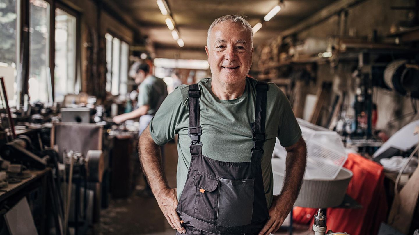 Älterer Mann in blauer Latzhose steht in der Werkstatt, ob er bis zur Rente mit 70 arbeitet?