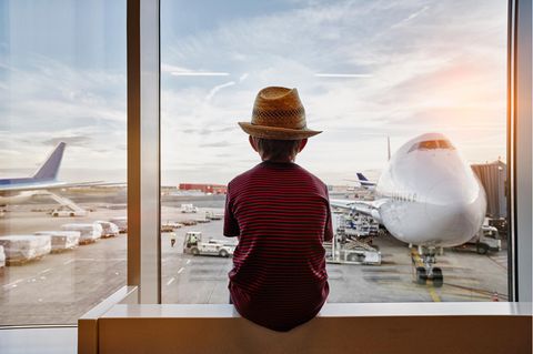 Junge schaut aus dem Fenster aus einem Flughafenterminal – die Flüge buchen mussten die Eltern