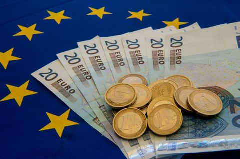 Euromünzen und -scheine auf einer EU-Flagge