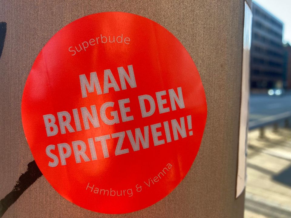 Aufkleber an einem Ampelmast mit dem Spruch "Man bringe den Spritzwein"