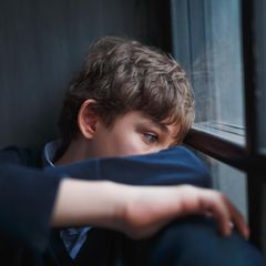 Ein Junge guckt traurig aus dem fenster
