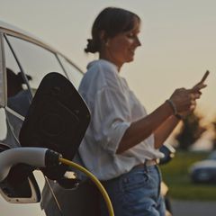 Frau in weißem Hemd lädt ihr E-Auto auf – negative Strompreise wären ihr sicher recht