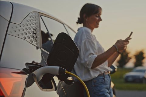 Frau in weißem Hemd lädt ihr E-Auto auf – negative Strompreise wären ihr sicher recht