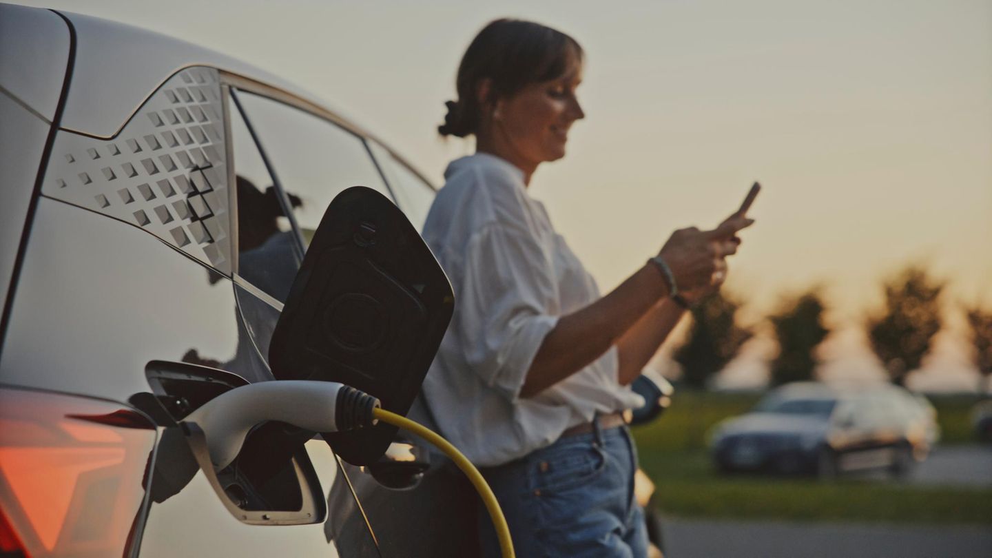 Frau in weißem Hemd lädt ihr E-Auto auf – negative Strompreise wären ihr sicher recht