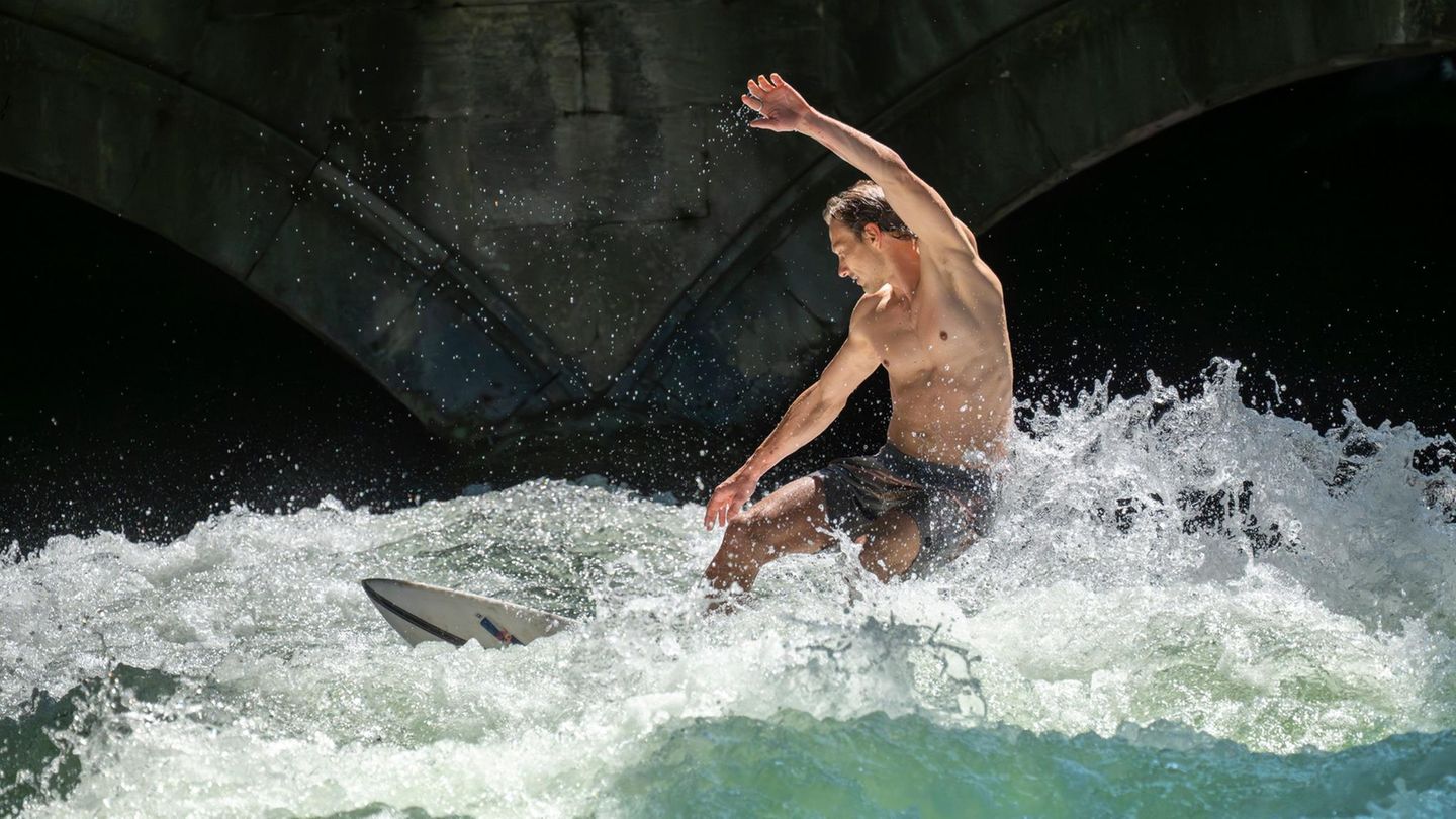 München, Deutschland. Patrick surft bei sommerlichen Temperaturen mit seinem Board auf der Eisbachwelle im Englischen Garten. Die Welle ist zu jeder Jahres- und Tageszeit ein Hotspot für Touristen und Surfer aus der ganzen Welt.