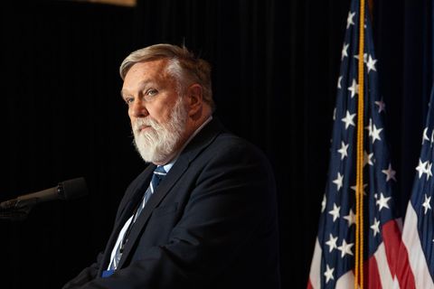 Doug Wilson steht an einem Mikrofon, neben ihm US-Flaggen