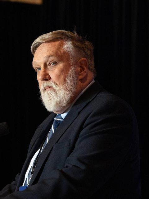 Doug Wilson steht an einem Mikrofon, neben ihm US-Flaggen