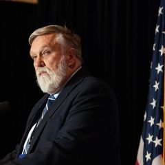 Doug Wilson steht an einem Mikrofon, neben ihm US-Flaggen