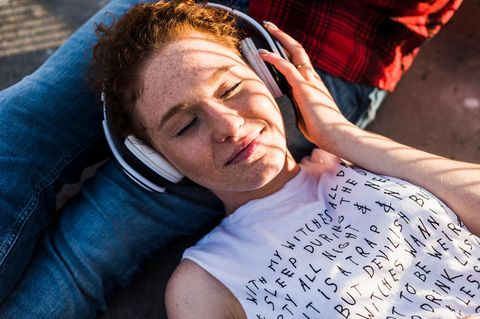 Eine junge Frau liegt auf dem Schoß ihres Freundes und hört Musik