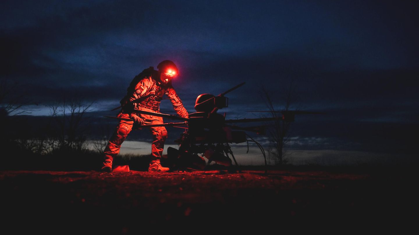 Ein Soldat der Ukraine bei Nacht, eine rote Lampe auf seinem Helm erleuchtet die Drohne, über die er sich beugt.