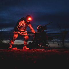 Ein Soldat der Ukraine bei Nacht, eine rote Lampe auf seinem Helm erleuchtet die Drohne, über die er sich beugt.