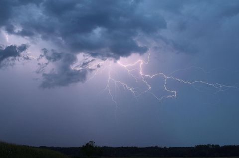 Ein Blitz zuckt bei einem Sommergewitter am abendlichen Himmel