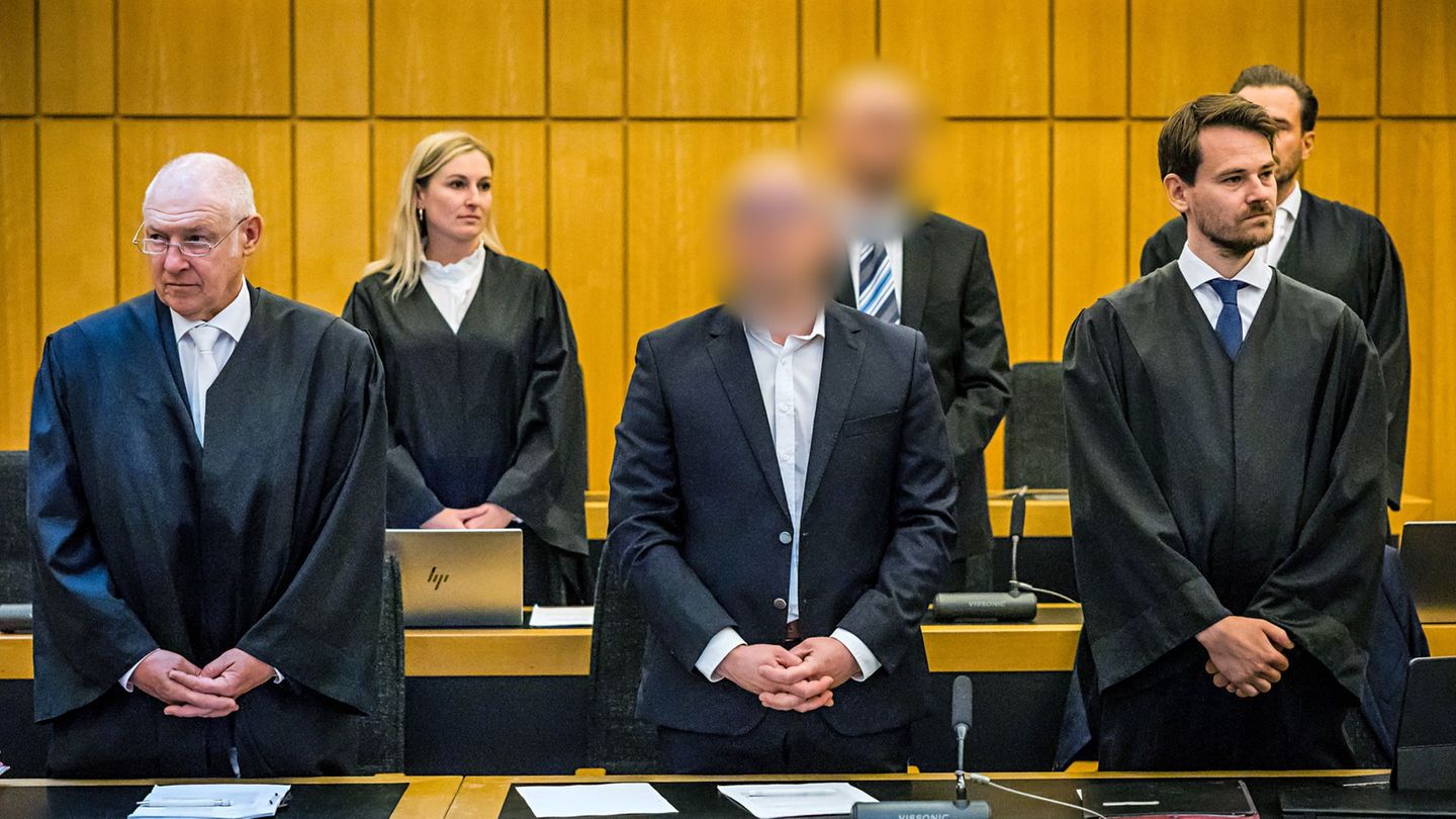 Die zwei angeklagten Brüder aus Oelde (vorne und hinten Mitte) stehen beim Einzug der Richter zwischen ihren vier Verteidigern.