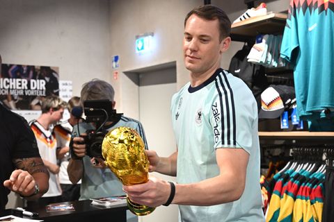 Lächelnd signiert Manuel Neuer einen goldenen WM-Pokal. Foto: Federico Gambarini/dpa
