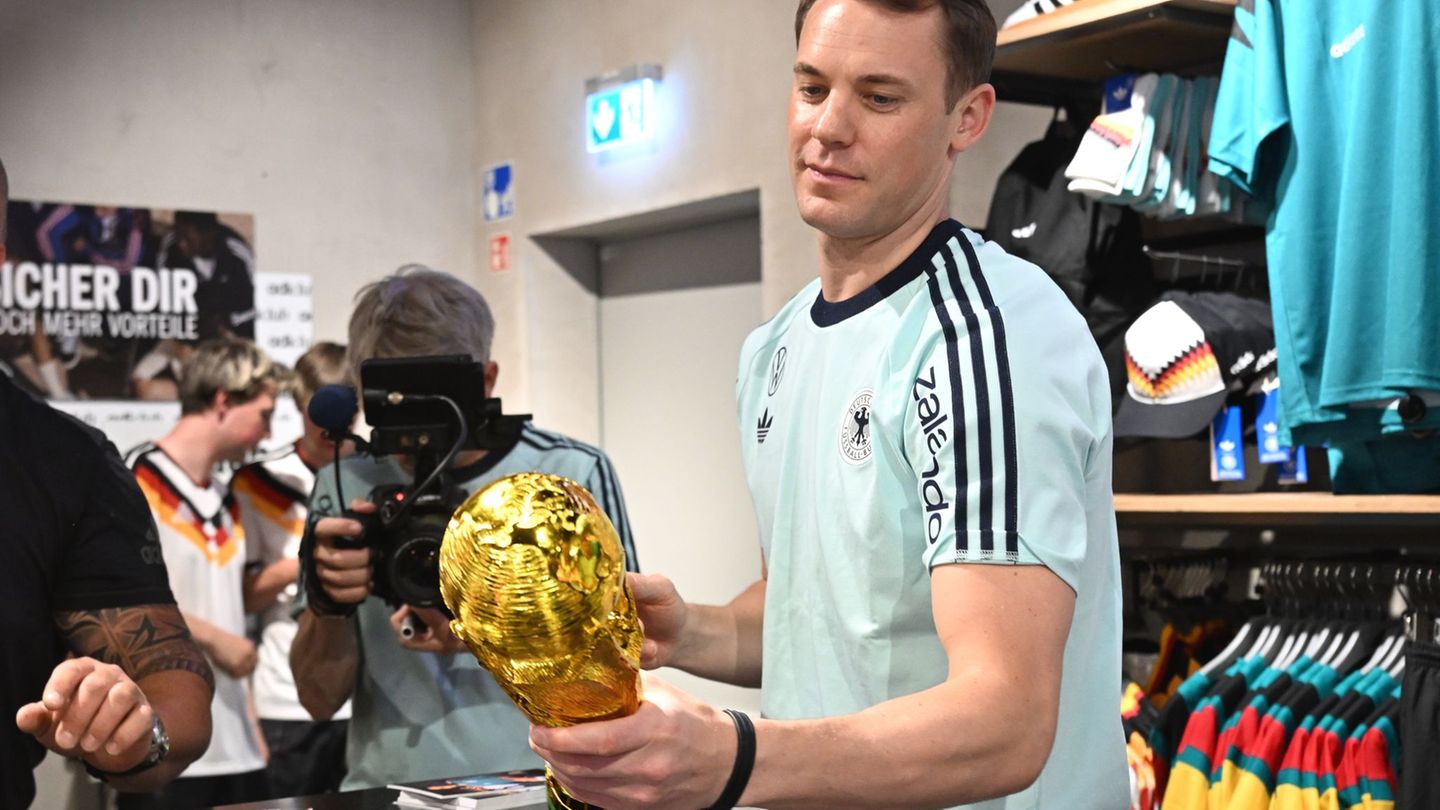 Lächelnd signiert Manuel Neuer einen goldenen WM-Pokal. Foto: Federico Gambarini/dpa