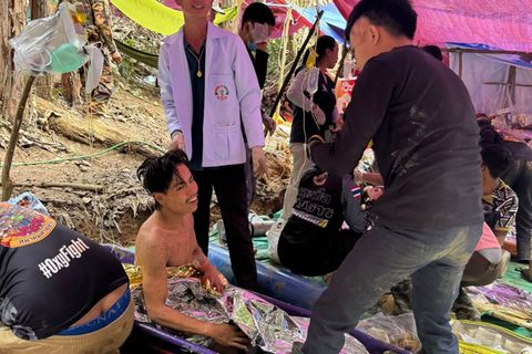Ein in eine Thermodecke gewickelter Mann sitzt unter einem Zeltdach, nachdem er der Höhle in Laos entkommen ist