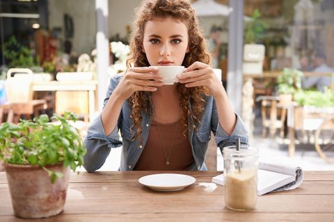 Symbolbild Single: Junge Frau sitzt allein im Kaffee und trinkt aus einer Tasse