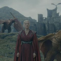 Rhaenyra Targaryen steht mit zwei Drachen an ihrer Seite vor einer Burg