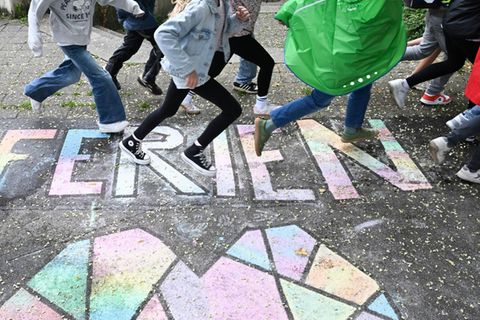 Grundschüler laufen am letzten Schultag vor den Sommerferien über einen bunten Kreide-Schriftzug „Ferien“