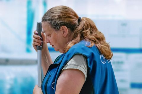 Eine Putzfrau in blauer Uniform hält die Stange eines Wischmopps fest – Szene des Films „Ich verstehe Ihren Unmut“