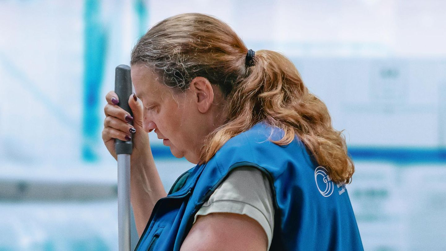 Eine Putzfrau in blauer Uniform hält die Stange eines Wischmopps fest – Szene des Films „Ich verstehe Ihren Unmut“