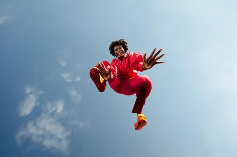 Eine Frau schwebt über der Kamera, sie lächelt. Im Hintergrund ist der Himmel zu sehen.